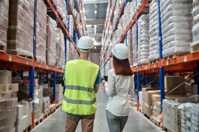 Back view of woman and man in warehouse aisle Подготовка на групажни пратки